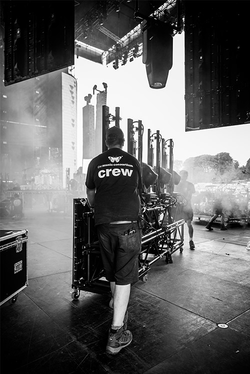 A stagehand pushing lighting gear onto a stage at a festival